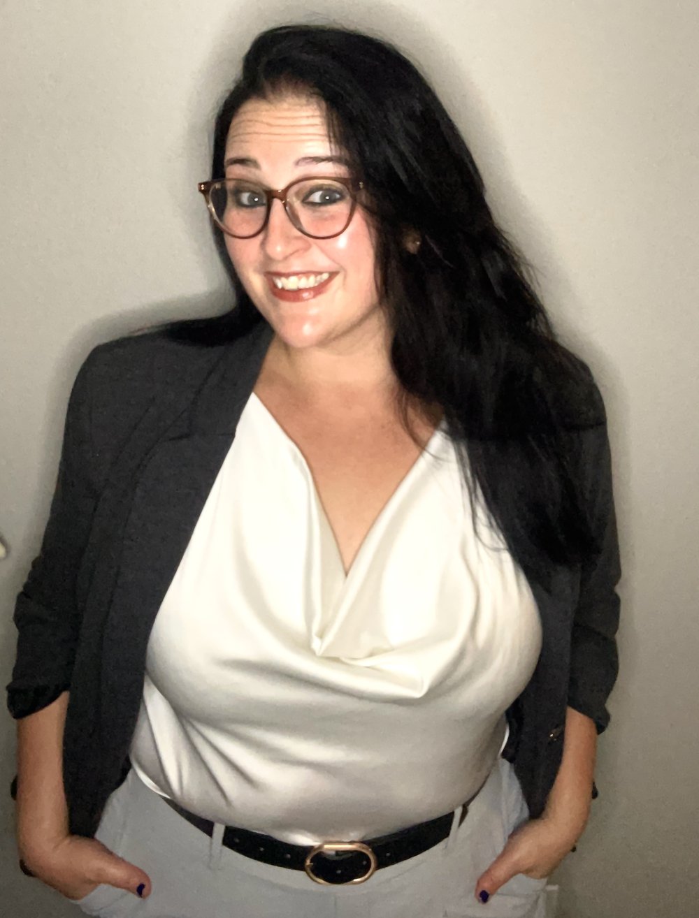 Katie smiling at the camera, wearing glasses, a white blouse and a dark blazer